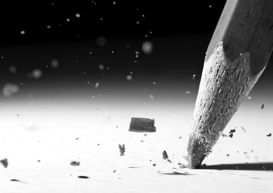 Pencil writing on hard surface with fragments of the pencil in the air.