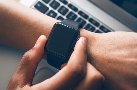 Smartwatch on wrist with laptop in the background.